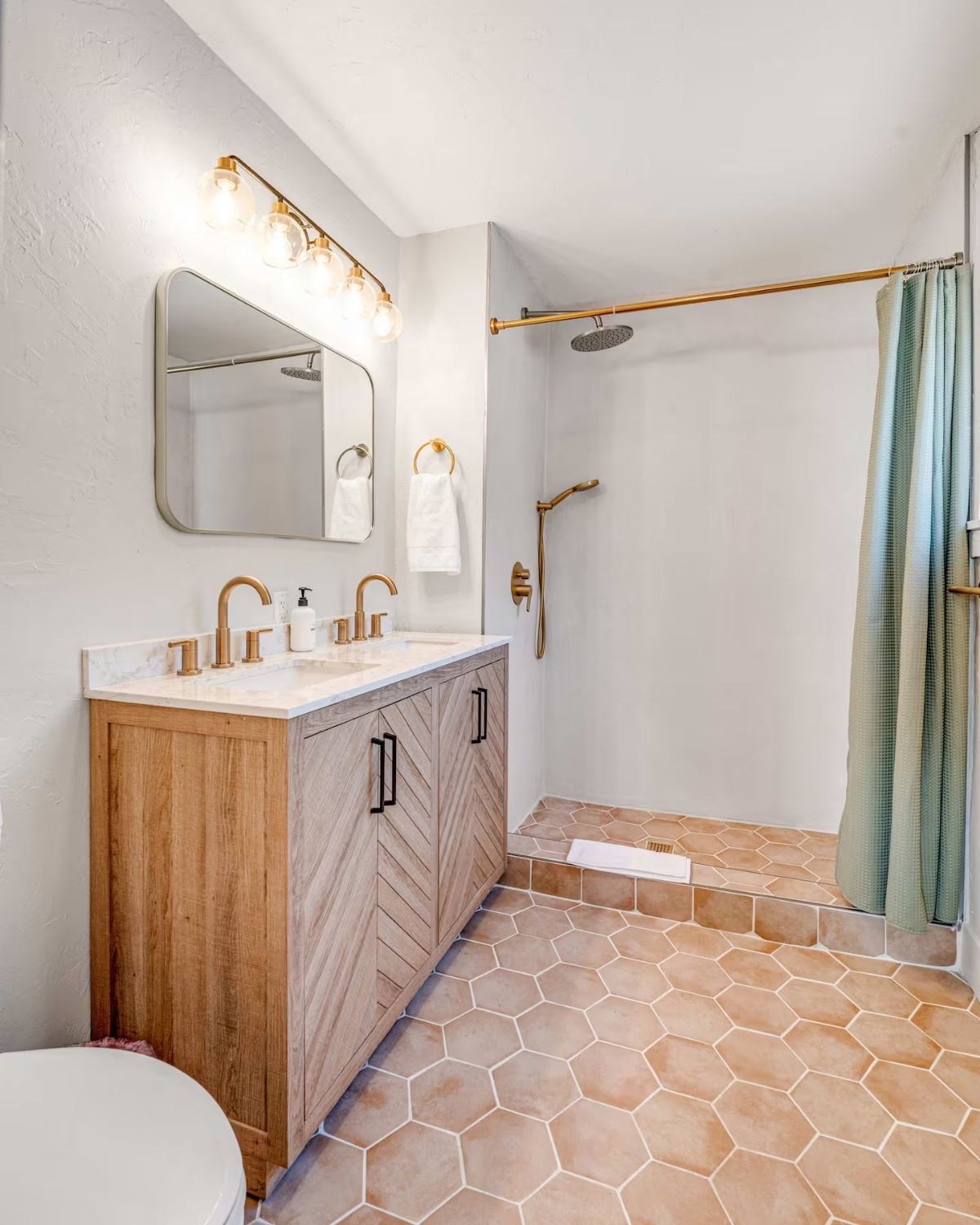 A restored casita bathroom: a walk-in shower with a rain head, brass fittings, a timber vanity and terracotta tile