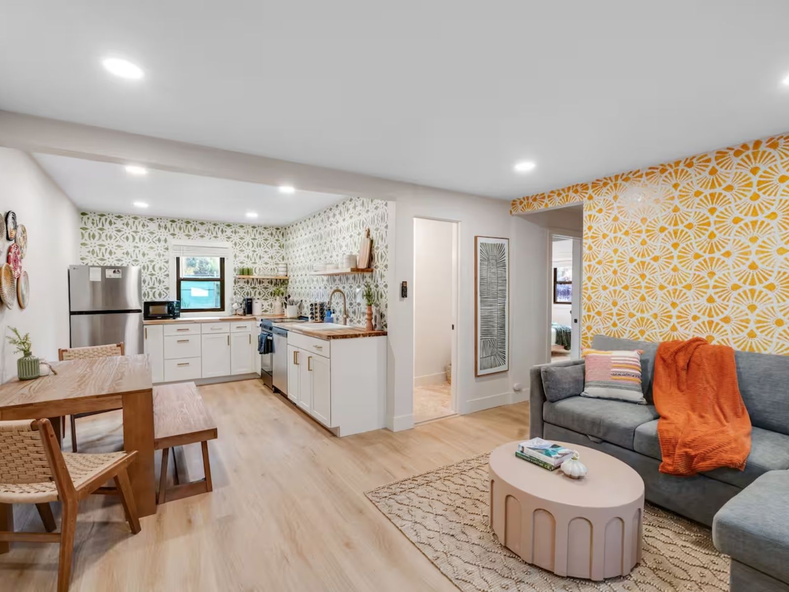 The open living space of a casita: a dining table and bench, a full kitchen with patterned tile, and a sofa under a sunburst papered wall
