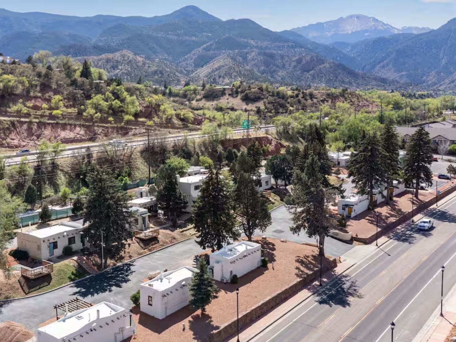 The whole property seen from the air: white adobe casitas set among pines on four acres, Manitou Avenue running along one side and the foothills and Pikes Peak beyond