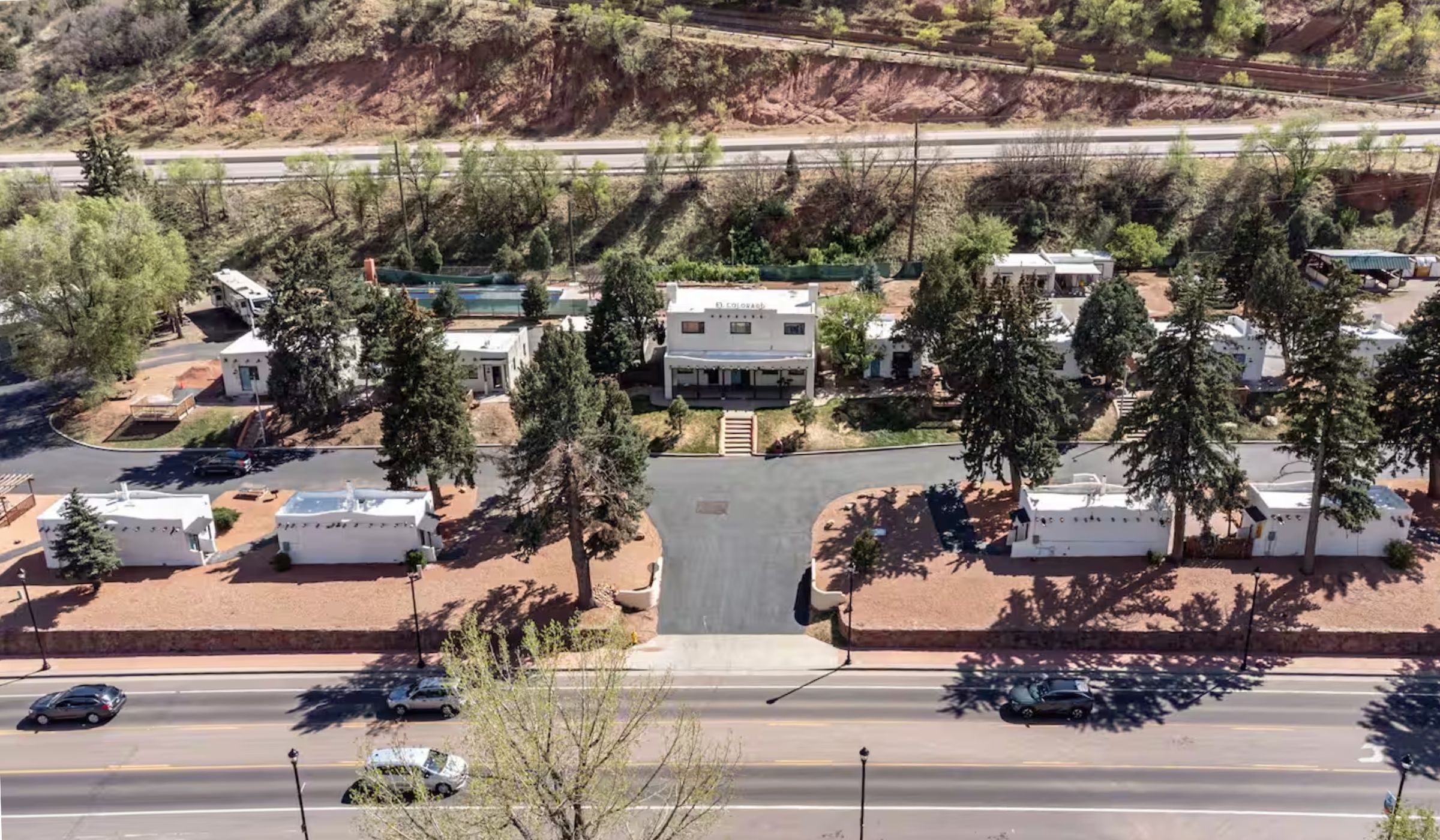 The property today, seen from above Manitou Avenue: the entrance drive climbing to the lodge, white adobe casitas ranged either side of it among the pines, and the rebuilt pool behind