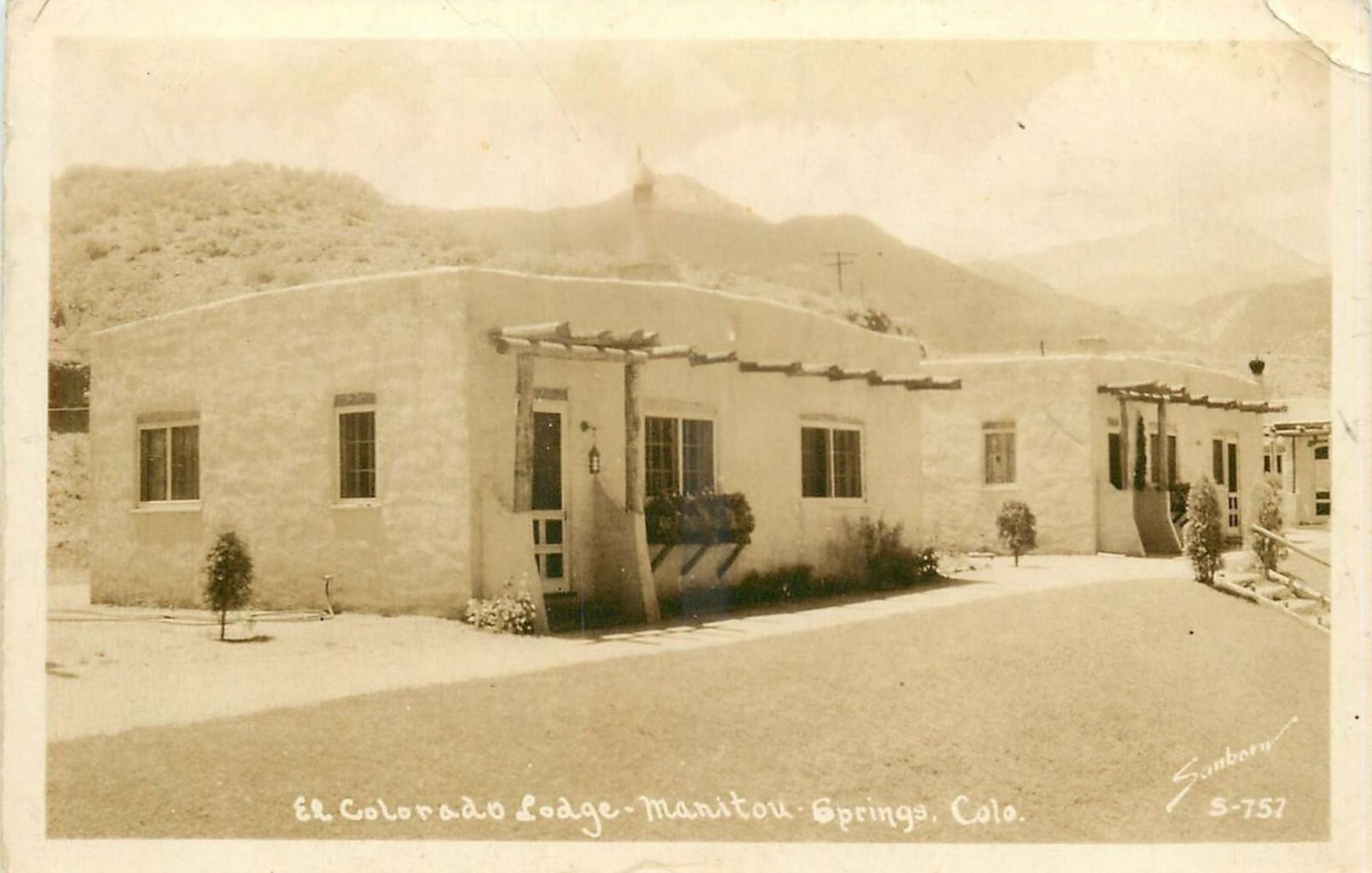 A period real-photo postcard captioned El Colorado Lodge, Manitou Springs, Colo., showing a run of adobe casitas with viga porches, a hillside rising behind them